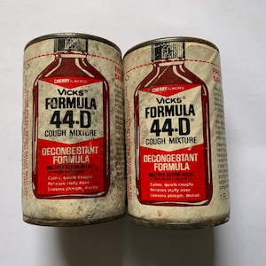 May include: Two vintage cans of Vicks Formula 44-D cough mixture. The cans are white with red and black text. The text on the cans reads "Vicks Formula 44-D Cough Mixture Decongestant Formula Multiple Action Relief Calms, quiets coughs Relieves stuffy nose Loosens phlegm, mucus".