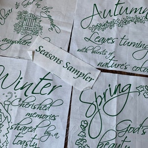 May include: Four white fabric squares with green embroidery depicting the four seasons. Each square features a different season with text describing the season. The text reads "Summer closer to God in the garden anywhere", "Autumn leaves turning with bursts of nature's color", "Winter cherished memories shared by a toasty fire", and "Spring God's beauty in the", with the word "Seasons Sampler" printed across the top.