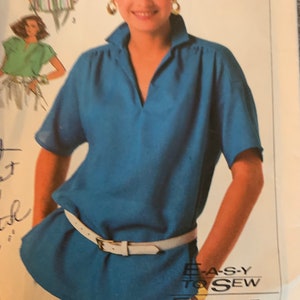 May include: A blue, short-sleeved blouse with a white belt and a v-neck collar. The text "EASY TO SEW" and "F-A-C-I-L-E A COUD" is printed on the bottom of the image.