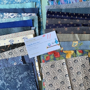May include: A collection of blue and white fabric scraps, some with floral patterns, arranged in two stacks. A business card with the text "Crafty By Nature Store" is visible in the center of the image.