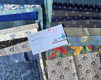 May include: A collection of blue and white fabric scraps, some with floral patterns, arranged in two stacks. A business card with the text "Crafty By Nature Store" is visible in the center of the image.