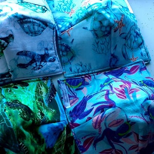 May include: Five fabric face masks with different sea life designs. The masks are all blue and green with white accents. The designs include sea turtles, coral, and fish.