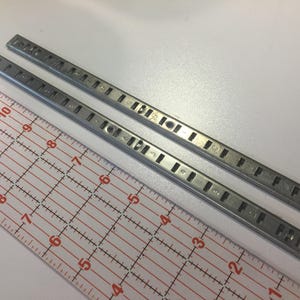 May include: Two silver metal shelf support rails with holes for shelf pins. The rails are 11 inches long and are measured against a ruler.