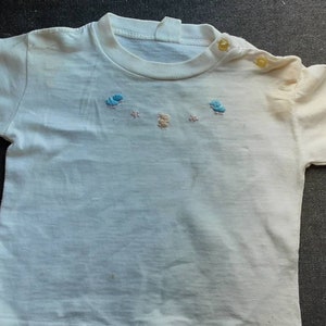 May include: A white short-sleeved t-shirt with blue and yellow embroidered flowers on the front.