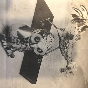 May include: A black and white photograph of a silver owl and rooster sculpture. The sculptures are made of many small, interlocking pieces. The owl is perched on a base, while the rooster is standing on a globe.