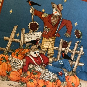May include: A blue and brown fabric with a fall theme. Two scarecrows are standing in front of a wooden fence with a sign that reads "Pumpkin Patch". There are pumpkins and gourds scattered around the scarecrows.