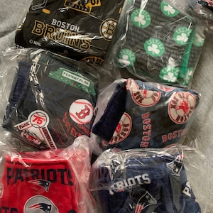May include: A collection of six fabric squares featuring different Boston sports team logos. The logos include the Bruins, Celtics, Red Sox, and Patriots. The squares are packaged in clear plastic bags.