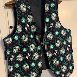 May include: A black vest with a repeating pattern of the Boston Celtics logo. The logo features a green shamrock, a basketball, and a basketball player in a green and white uniform. The vest has a black lining and a small tag that reads "nail alyn".