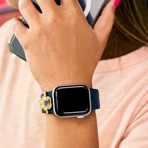 Pu&ograve; includere: Un Apple Watch nero con un cinturino blu navy e un ciondolo a forma di zampa d'oro. Il quadrante dell'orologio &egrave; nero e il cinturino &egrave; realizzato in un materiale morbido e flessibile.