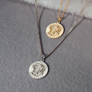 May include: Two gold necklaces with Saint Michael pendants. The pendants feature a depiction of Saint Michael slaying a demon, with the words "Saint Michael Protect Us" inscribed around the edge.