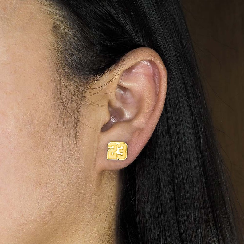 May include: Gold-coloured earring with the number 23 in a block font.