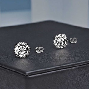 May include: A pair of silver firefighter earrings with a fire department logo. The logo features a fireman holding an axe and a hose, with the words "FIRE DEPT" around the outside.