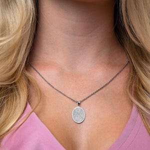 Puede incluir: Un collar de cadena de plata con un colgante redondo que presenta un dise&ntilde;o de huella digital detallado.