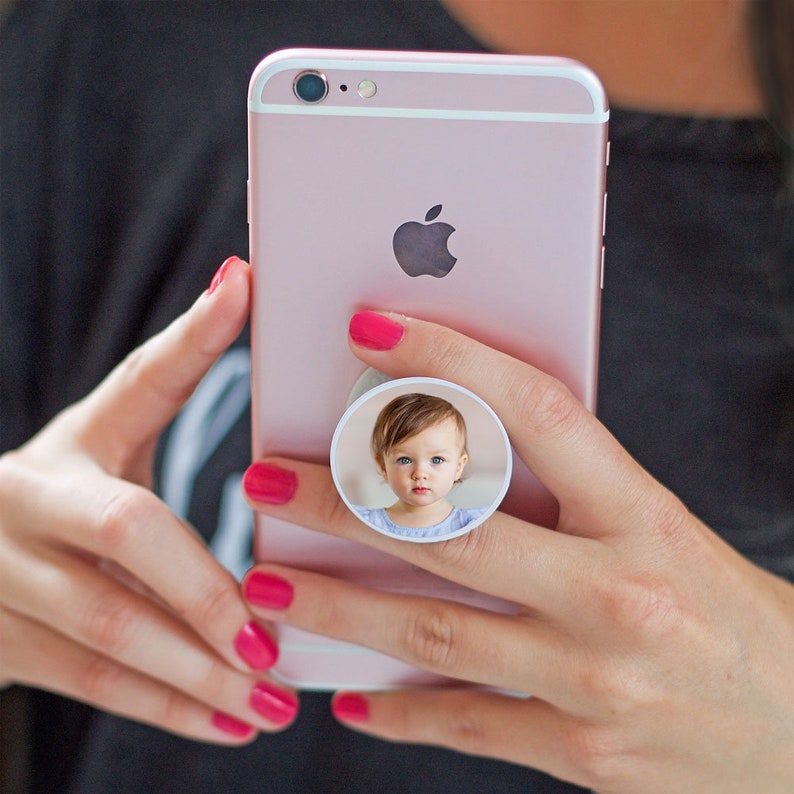 K&ouml;nnte beinhalten: Ein rosa iPhone mit einem wei&szlig;en Handygriff mit einem Foto eines kleinen M&auml;dchens mit braunen Haaren und blauen Augen.