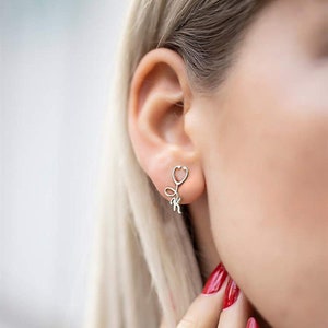 May include: Silver stethoscope earrings with a small letter 'K' charm hanging from the bottom.