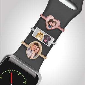 Pu&ograve; includere: Un Apple Watch nero con un cinturino nero. Il cinturino ha tre diversi accessori per foto: un accessorio a forma di cuore con una foto di due ragazze, un accessorio rettangolare con una foto di un gatto e un cane e un accessorio ovale con una foto di una coppia.
