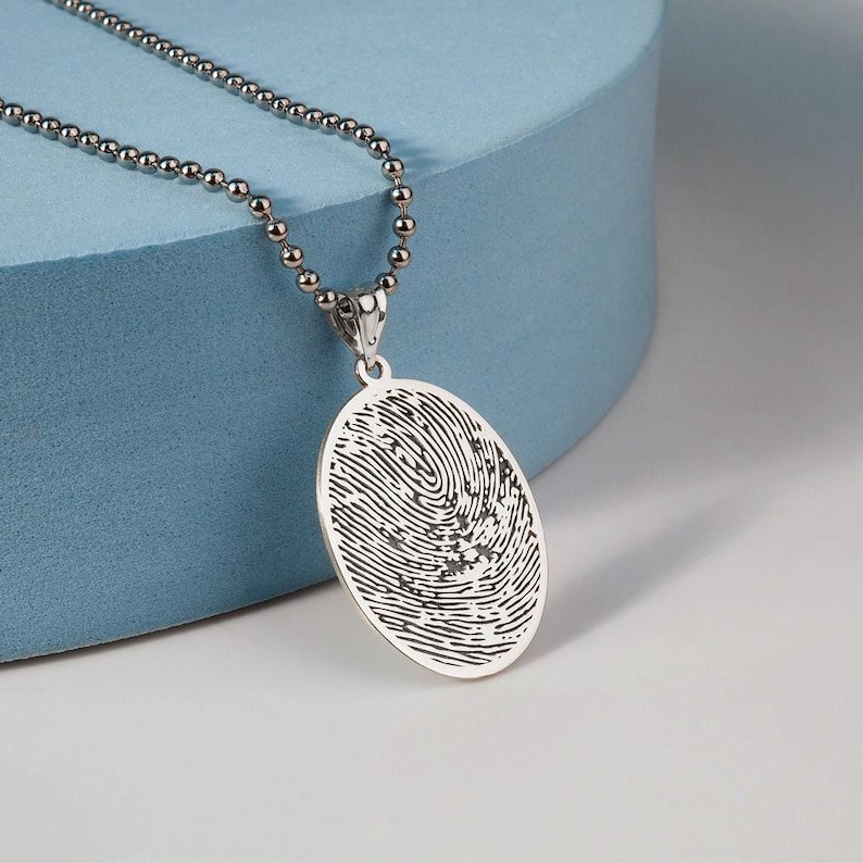 Puede incluir: Collar de plata con un colgante redondo con un dise&ntilde;o de huella digital detallado.