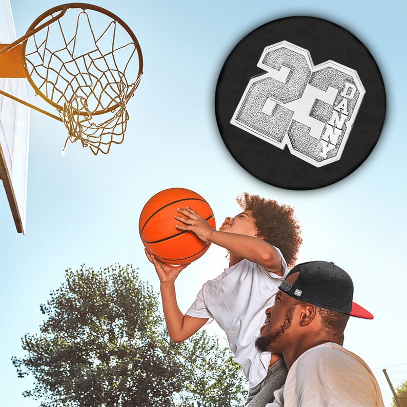 K&ouml;nnte beinhalten: Ein Vater und sein Sohn spielen Basketball. Der Sohn tr&auml;gt ein wei&szlig;es Hemd und h&auml;lt einen Basketball. Der Vater tr&auml;gt eine schwarze Baseballkappe und ein wei&szlig;es Hemd. Der Sohn springt hoch, um den Ball in den Korb zu werfen. Der Korb ist im Hintergrund. Der Vater h&auml;lt die Beine seines Sohnes. Der Sohn l&auml;chelt. Der Vater schaut seinen Sohn an. Der Basketball hat ein schwarz-wei&szlig;es Design mit der Nummer 22 und dem Namen Danny.