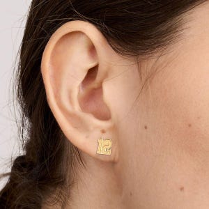 May include: Gold-toned number 12 earrings. The earrings are small and feature a blocky font style.