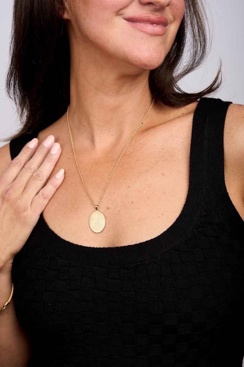Puede incluir: Un collar de cadena de oro con un gran colgante ovalado. El colgante es liso y tiene una superficie ligeramente texturizada.