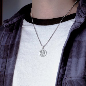 May include: A silver chain necklace with a round pendant featuring the words "Saint Michael Protect Us" and a depiction of an angel.