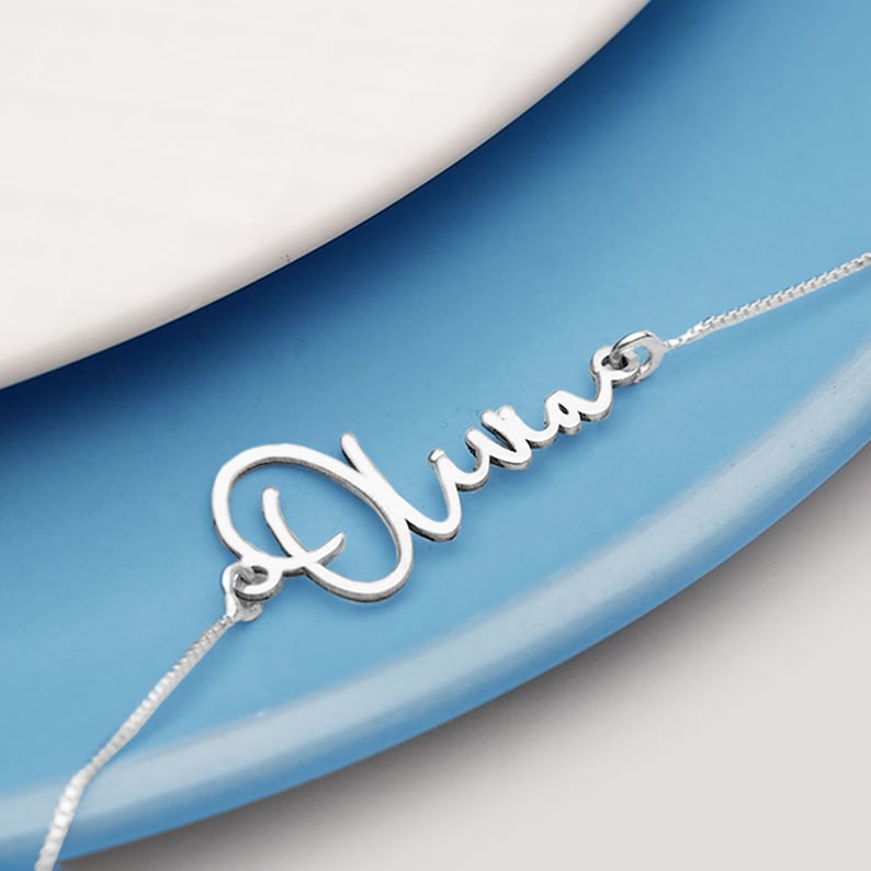 Peut inclure: Un collier en argent avec le nom "Olivia" &eacute;crit en cursive.