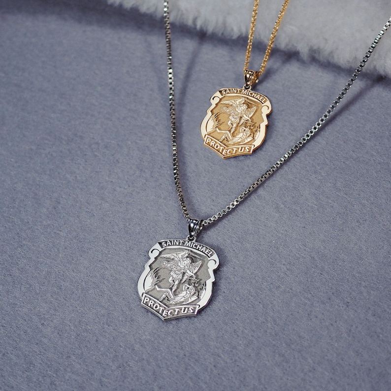 K&ouml;nnte beinhalten: Zwei silberne Ketten mit Anh&auml;nger von Sankt Michael. Die Anh&auml;nger zeigen eine Darstellung des Heiligen Michael, der einen D&auml;mon besiegt, mit den Worten "Saint Michael" und "Protect Us" auf dem Anh&auml;nger.