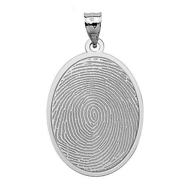 Puede incluir: Un colgante ovalado de plata con un dise&ntilde;o de huella digital detallado.