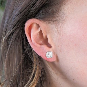 May include: Silver stud earrings with the number 48 in white lettering.