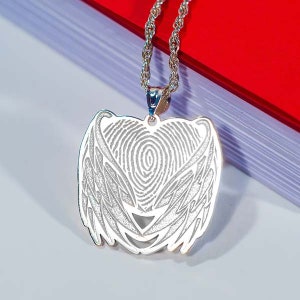May include: Silver pendant necklace with a heart-shaped design featuring a fingerprint inside and angel wings on either side.