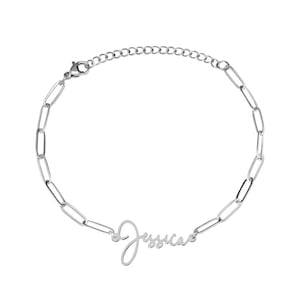 Può includere: Un braccialetto color argento con un design a maglie di catena e il nome "Jessica" in corsivo. Il braccialetto ha una chiusura a moschettone. Il gioiello è presentato su uno sfondo bianco.