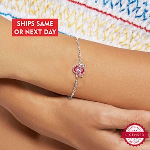 Peut inclure: Un bracelet à chaîne argentée avec un charm en forme de logo de l'Université d'État de l'Ohio, rouge et blanc. Le charm représente une lettre "O" stylisée avec "OHIO STATE" écrit dessus. Le bracelet est sur un poignet. Le texte "SHIPS SAME OR NEXT DAY" est dans un encadré rouge.