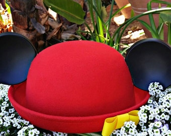 May include: A red felt hat with black felt ears. The hat is sitting on a bed of white flowers.