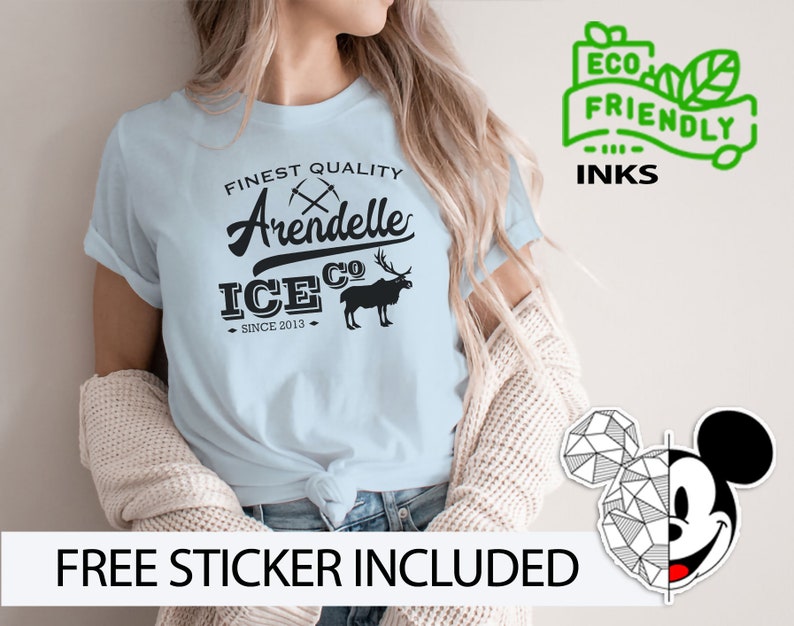 May include: Light blue t-shirt with a black graphic design that says "Finest Quality Arendelle Ice Co. Since 2013". The graphic also includes a stylized image of a moose and crossed pickaxes. The t-shirt is being modeled by a person. The text "ECO FRIENDLY INKS" is in a green box with a leaf design.