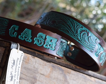 May include: Two brown leather belts with turquoise tooled designs. One belt has the word "CASH" embossed on it. A white tag with the text "Outlaw Leather USA Handmade by Nez" is visible.