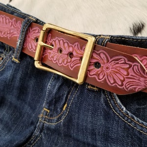 May include: A brown leather belt with a pink floral design and a gold buckle.