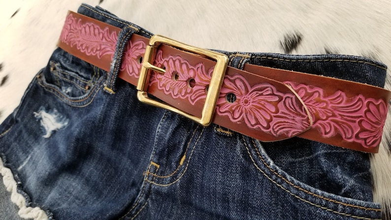 May include: A brown leather belt with a pink floral design and a gold buckle.
