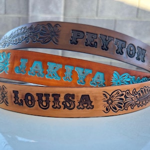 May include: Three leather belts with floral designs and personalized names: Peyton, Jakiya, and Louisa. The belts are brown with turquoise blue lettering.