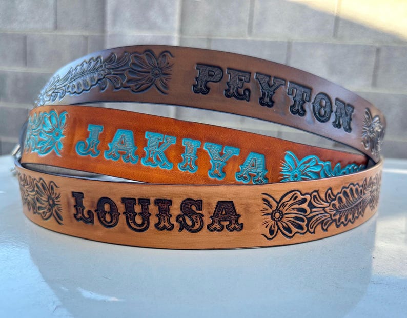 May include: Three leather belts with floral designs and personalized names: Peyton, Jakiya, and Louisa. The belts are brown with turquoise blue lettering.