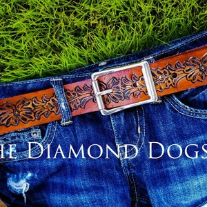 May include: A brown leather belt with a floral design and a silver buckle. The belt is worn on a pair of blue denim shorts. The text "THE DIAMOND DOGS" is visible below the belt.
