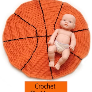 Könnte beinhalten: Eine gehäkelte orangefarbene und schwarze Babydecke in Basketballform mit einer Puppe darauf. Der Text "Crochet Pattern" ist auf einem orangefarbenen Rechteck unter der Decke gedruckt.