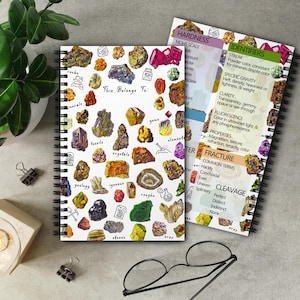 May include: A spiral-bound notebook with a cover featuring colorful illustrations of various rocks and minerals, labeled with terms like "fossils" and "crystals." A reference card on hardness and identifiers is visible. The notebook has the text "This Belongs To:" on the cover.