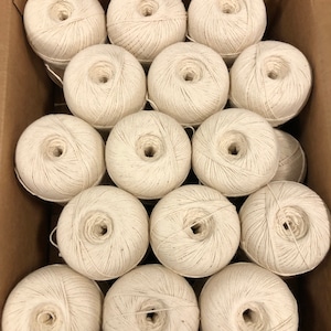 May include: A box filled with 14 balls of white yarn. The yarn is wound into balls and is ready for knitting or crocheting.