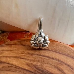 May include: Silver pendant featuring a lotus flower design with a stylized swirl in the center. The pendant has a loop at the top for attaching to a chain.