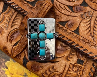 May include: A silver cross with turquoise stones set in a checkered background. The cross is on a brown leather background with an embossed floral pattern.