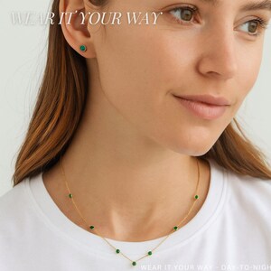 K&ouml;nnte beinhalten: Eine goldene Halskette mit gleichm&auml;&szlig;ig verteilten, runden, in Zargenfassung gefassten gr&uuml;nen Steinen sowie ein passender einzelner Ohrstecker mit gr&uuml;nem Stein. Der Text WEAR IT YOUR WAY steht oben links, WEAR IT YOUR WAY - DAY-TO-NIGHT unten.