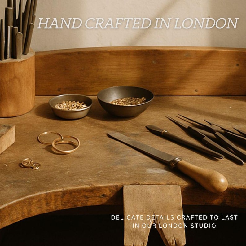 K&ouml;nnte beinhalten: Eine h&ouml;lzerne Juwelierwerkbank mit zwei kleinen Metallschalen voller Goldteile, drei Goldringen und verschiedenen Metallfeilen mit Holzgriffen. Der Text lautet HAND CRAFTED IN LONDON und DELICATE DETAILS CRAFTED TO LAST IN OUR LONDON STUDIO.
