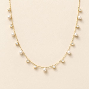 May include: A gold chain necklace featuring a delicate arrangement of alternating round white pearls and clear, bezel-set circular crystals suspended along the length of the chain, creating a balanced and symmetrical jewelry design.