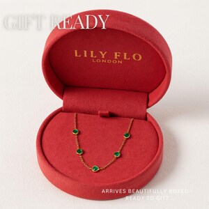 May include: A gold chain necklace featuring five small, round, green bezel-set stones, presented in a round red velvet jewelry box. The interior lid is printed with the text LILY FLO LONDON and the text GIFT READY is visible at the top.