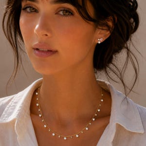 May include: A gold chain necklace featuring evenly spaced small white pearl charms hanging from the links. The necklace is paired with a matching stud earring that displays a single white pearl and a small pink stone set in a gold metal base.